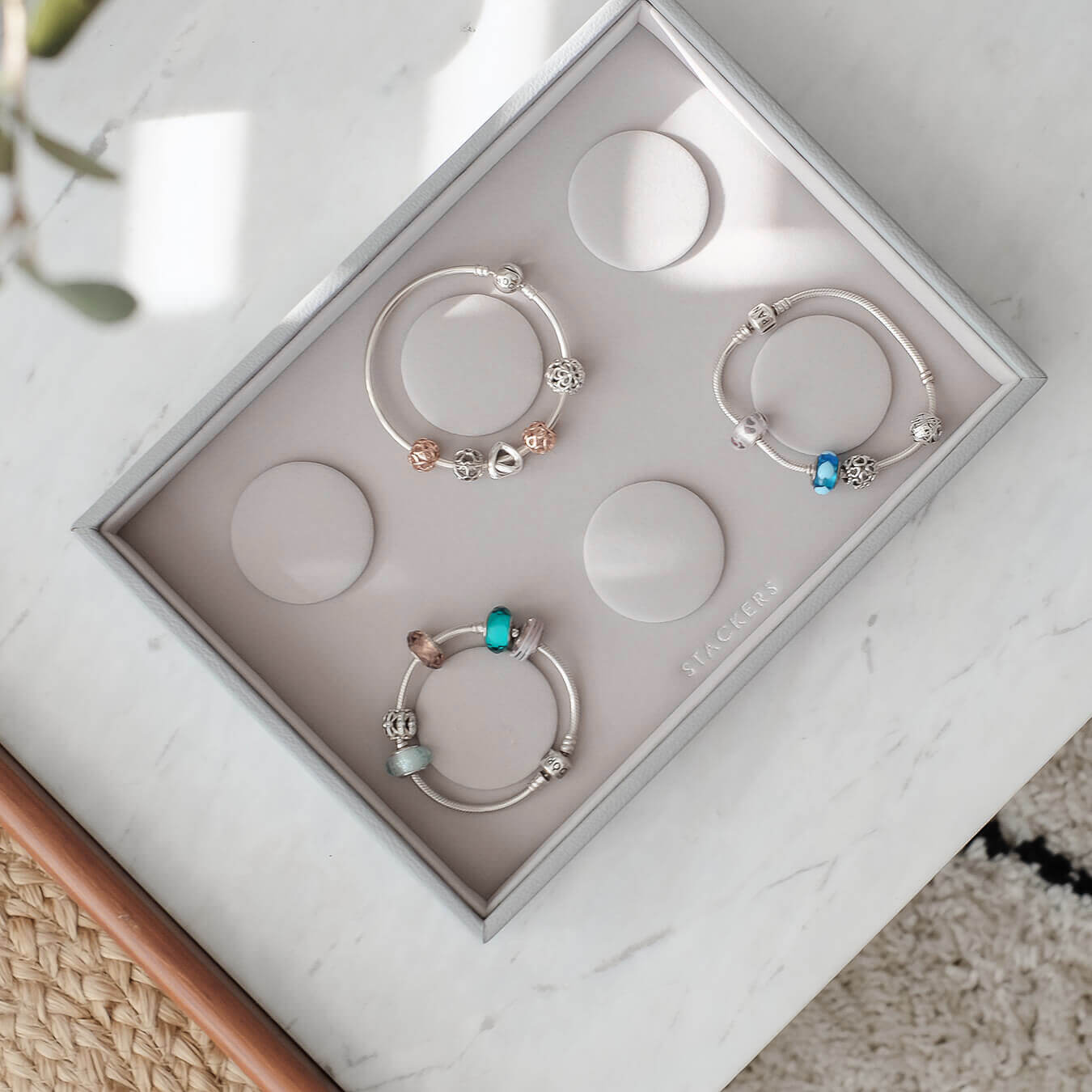 Three silver bracelets with colorful beads in a box on a marble surface.
