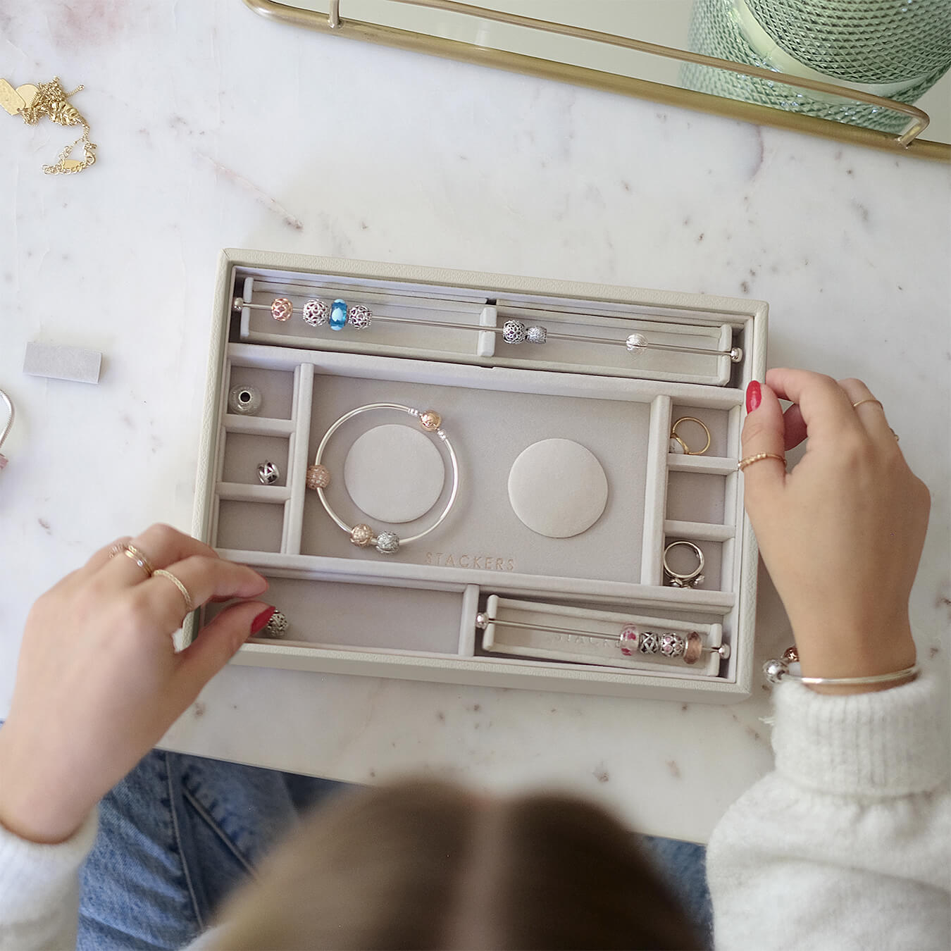 Person organizing jewelry in an open jewelry box on a marble surface.