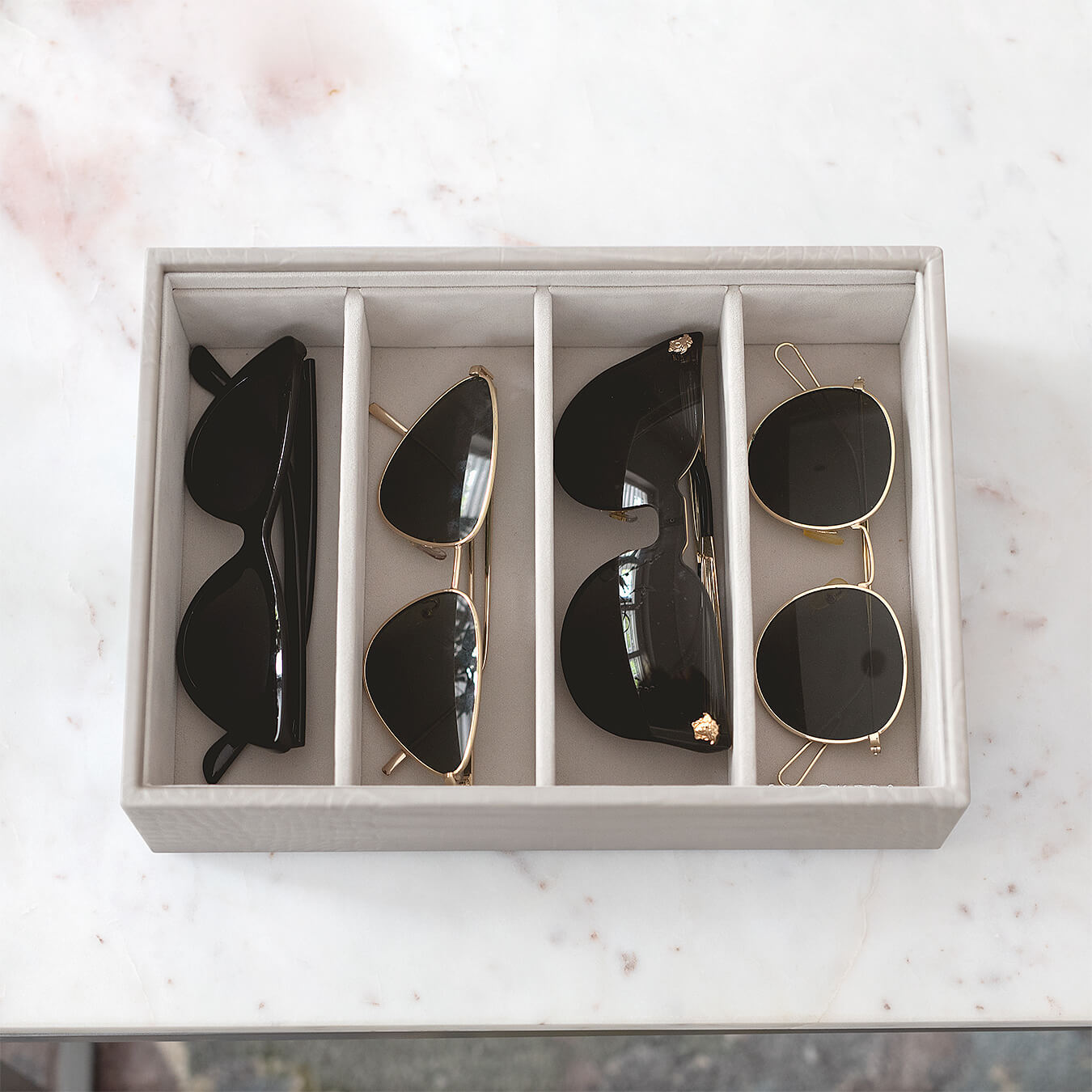 putty croc storage tray with four compartments, each holding one pair of sunglasses.