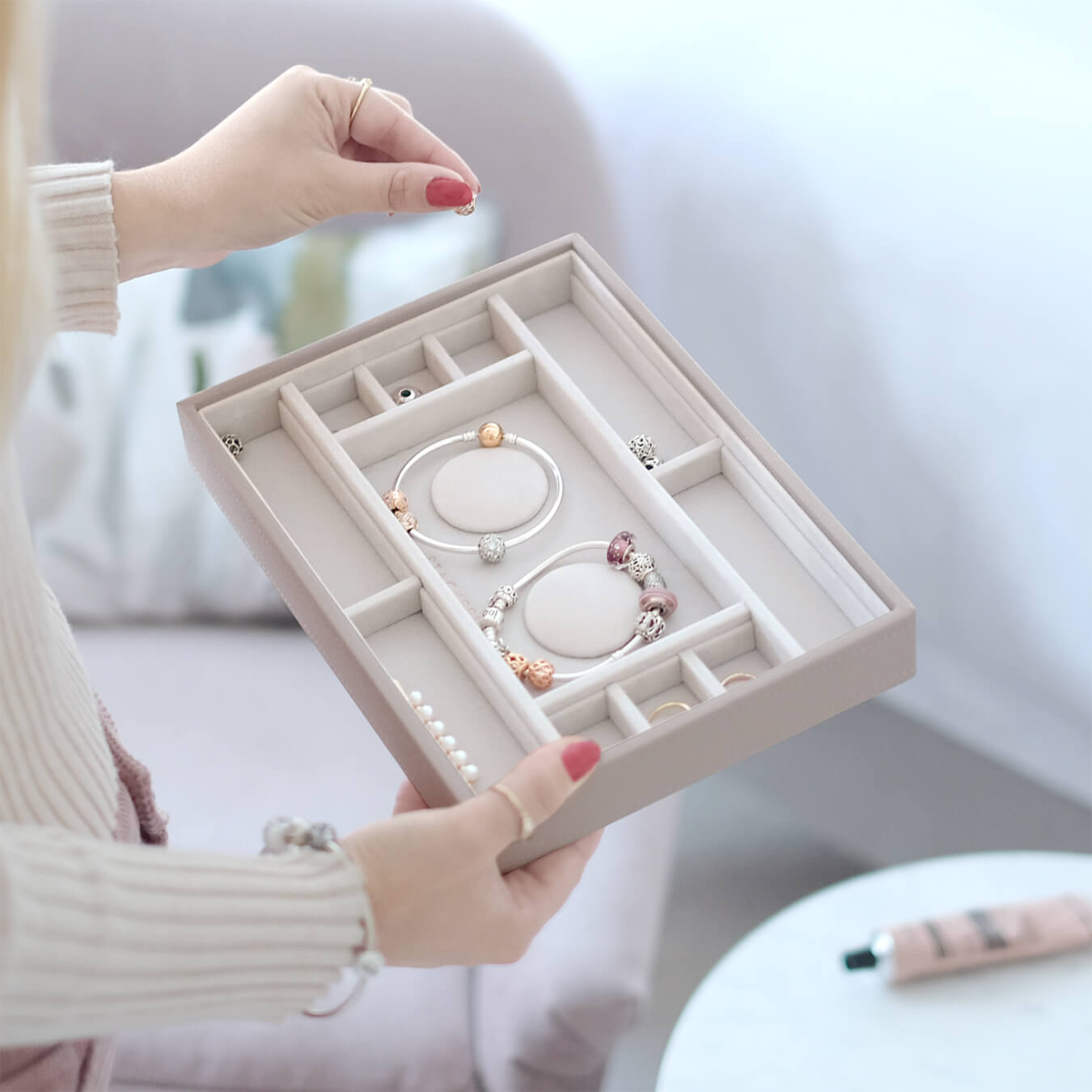 Jewelry box with bracelets held by a person with red nail polish.