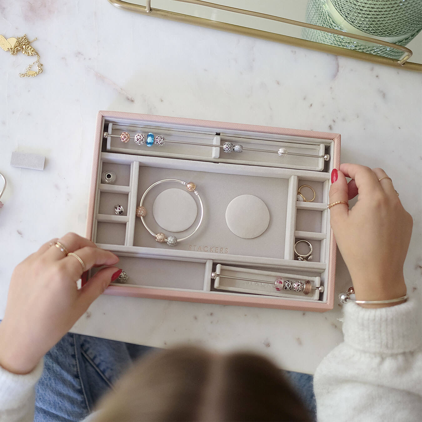 Person organizing jewelry in a pink jewelry box on a marble surface.