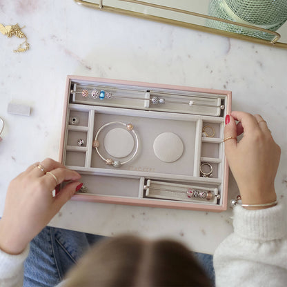 Person organizing jewelry in a pink jewelry box on a marble surface.