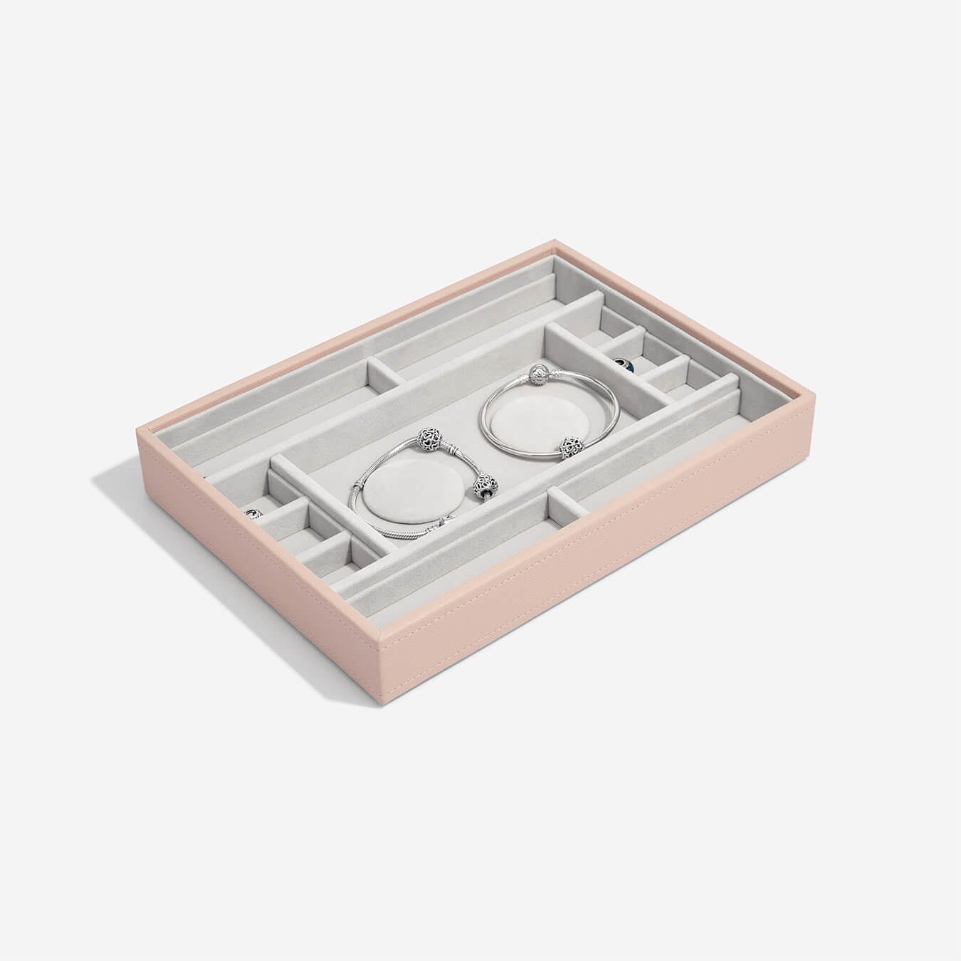 Pink jewelry box with compartments holding silver earrings on a white background