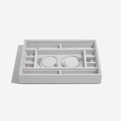 Pebble grey jewelry organizer with compartments holding silver bracelets on a white background