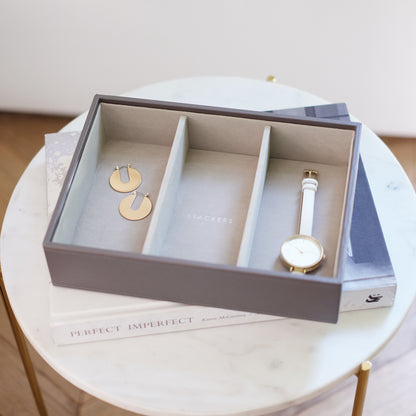 Jewelry set including earrings and a watch in an open jewelry box on a round table.