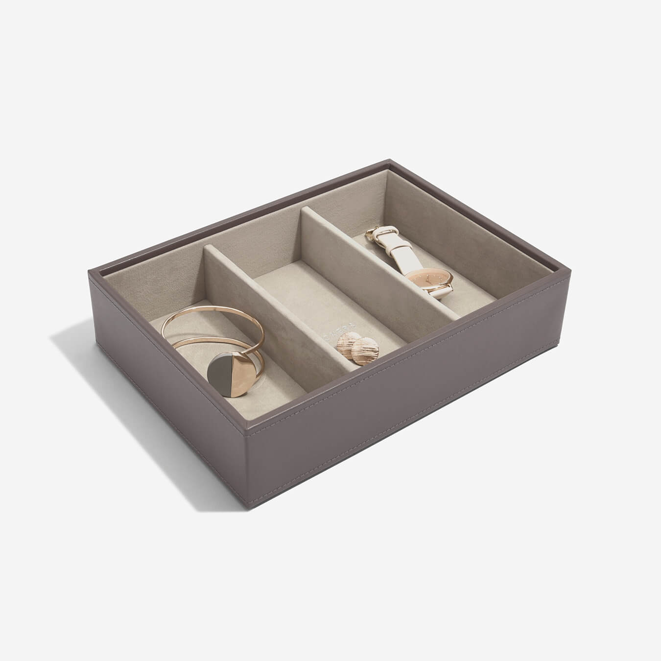 Mink coloured jewelry box with compartments containing a bracelet, ring, and watch on a white background