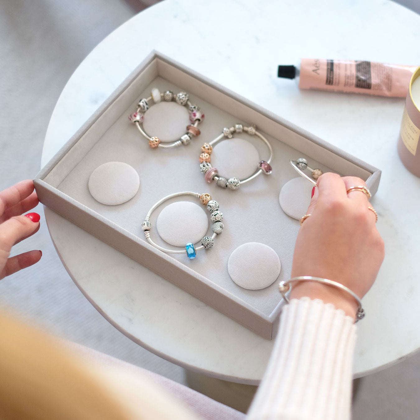 Person arranging beaded bracelets in a box on a white surface