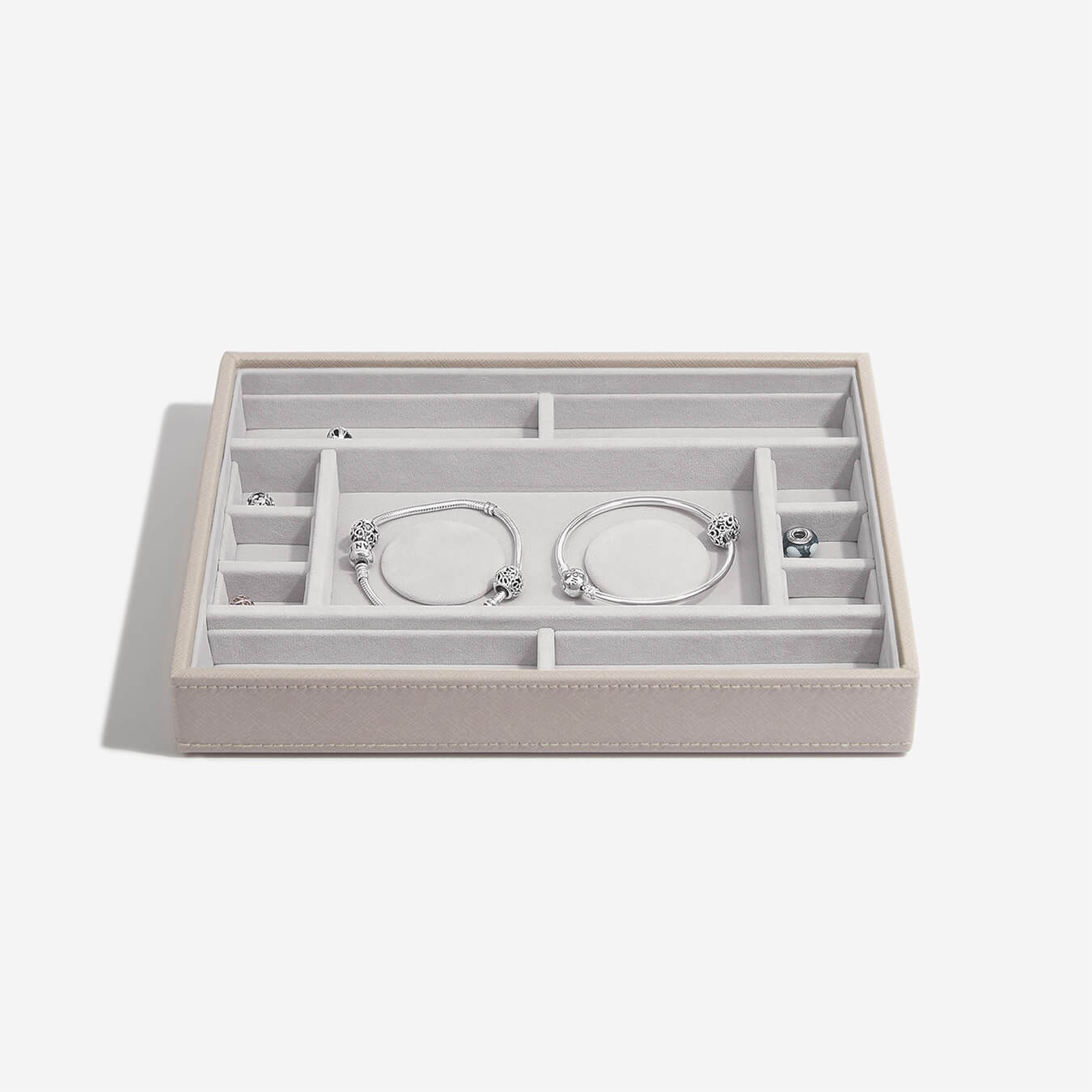 Taupe jewelry box with compartments holding silver bracelets on a white background