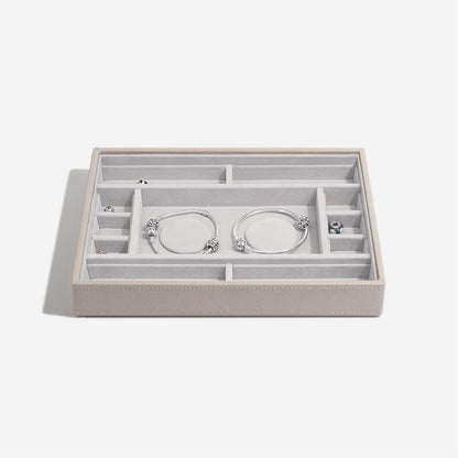 Taupe jewelry box with compartments holding silver bracelets on a white background