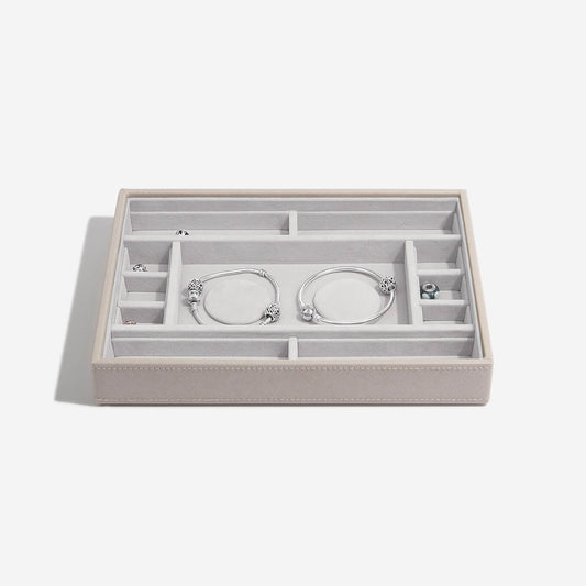 Taupe jewelry box with compartments holding silver bracelets on a white background