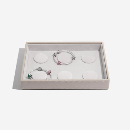 Two silver bracelets with charms in a box on a light gray background