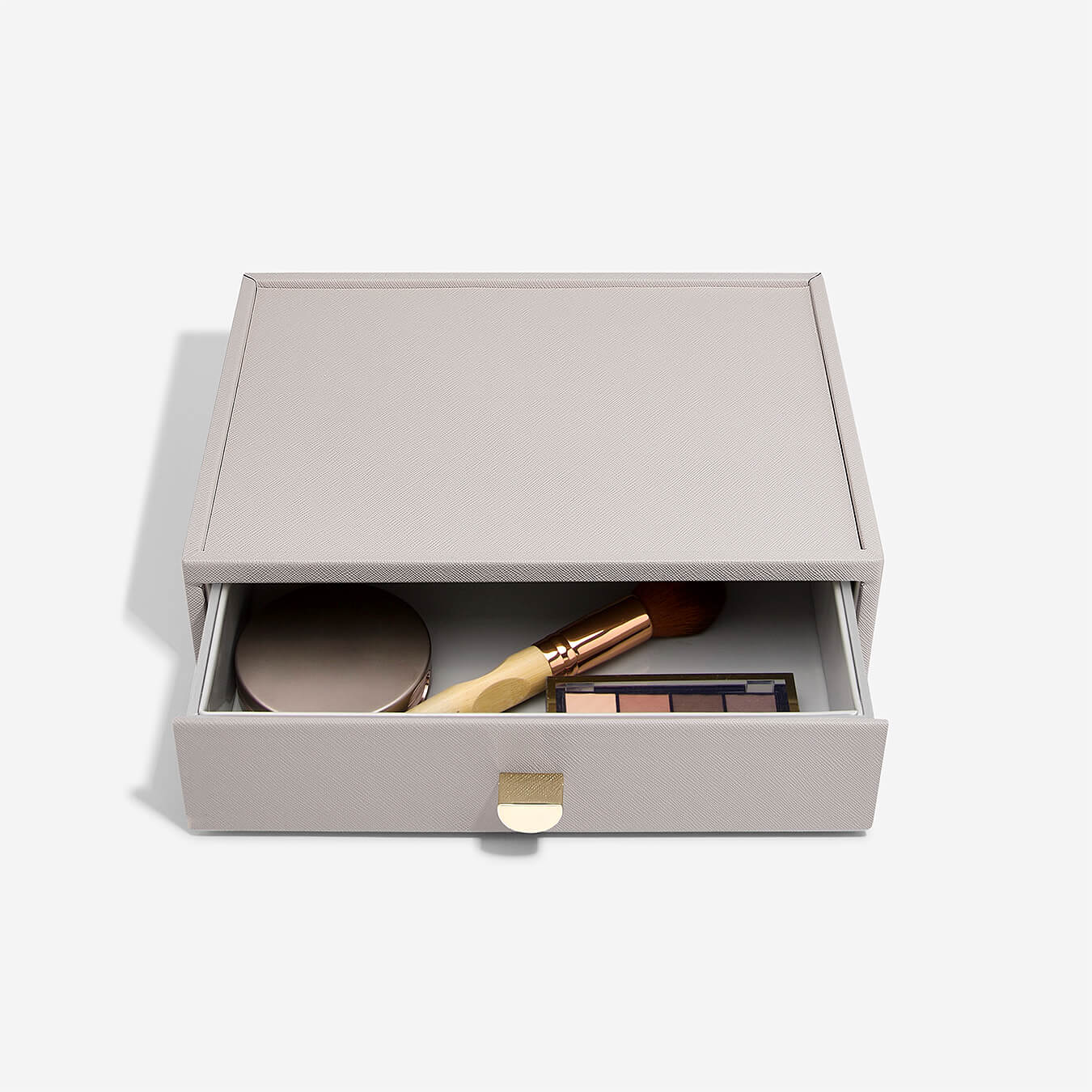 Taupe box with makeup items in a drawer on a white background